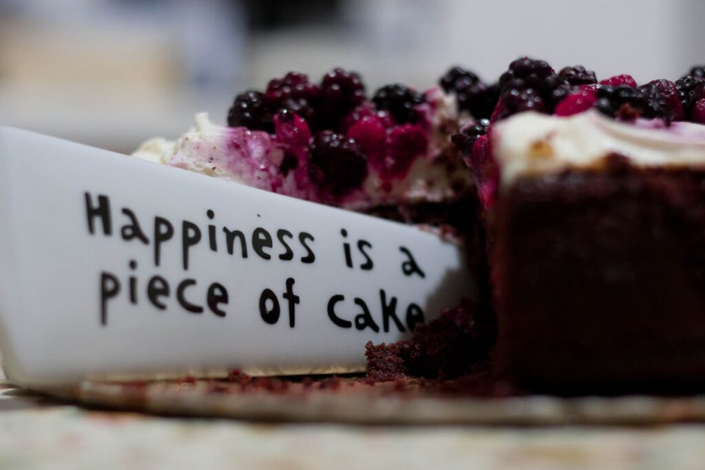 Slice of berry-topped cheesecake with a message plate saying 'Happiness is a piece of cake'.