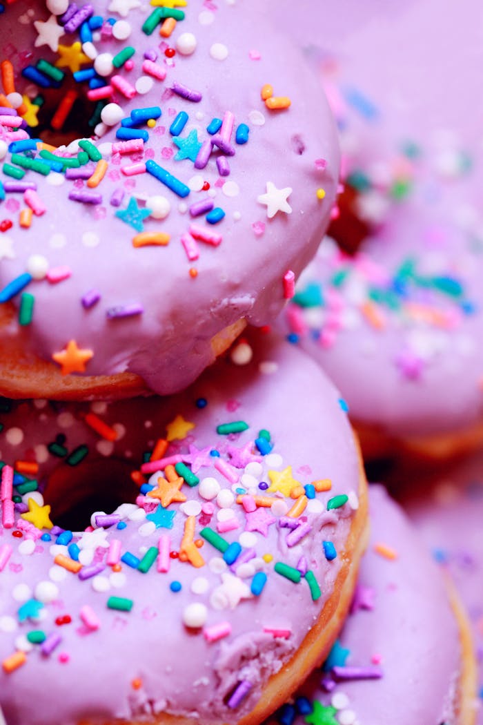 A close-up of vibrant donuts with purple icing and colorful sprinkles.