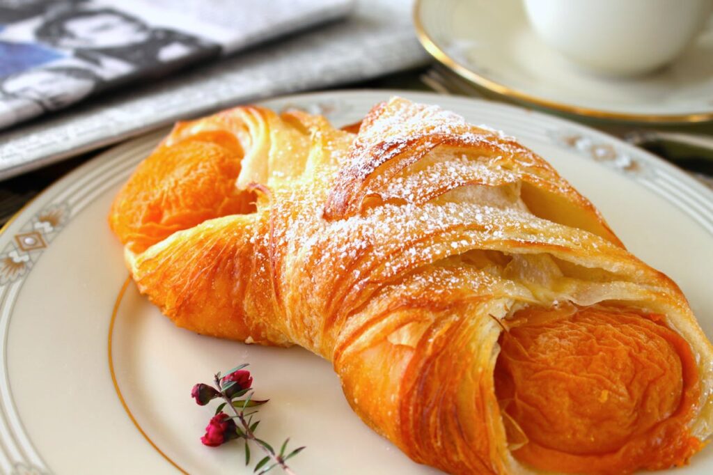 A delicious croissant filled with apricot on a decorative plate, perfect for breakfast delight.